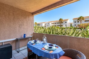 A balcony with a table set for two, overlooking a residential area with buildings and palm trees. - La Plage d'Irène (Appartement n°36) - Avec balcon (San-Nicolao)