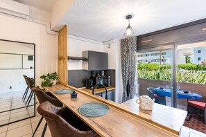 A modern kitchen with a wooden dining table, chairs, and a hanging light fixture. - La Plage d'Irène (Appartement n°36) - Avec balcon (San-Nicolao)