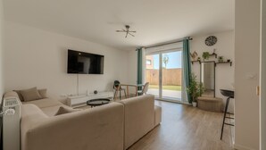 Ein modernes Wohnzimmer mit Flachbildfernseher, einer Couch, einem Esstisch und einer Schiebeglastür, die zu einem Außenbereich führt.