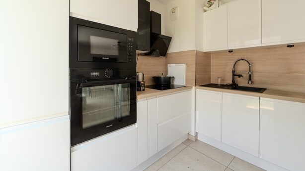 Eine moderne Küche mit weißen Schränken, einem schwarzen Backofen, einer Mikrowelle und einer Holzrückwand.