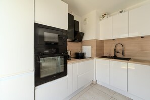 Une cuisine moderne avec des meubles blancs, un four noir, un four à micro-ondes et un pare-feu en bois.