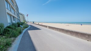 A paved walkway beside a beach with a building on the left. - La Plage - À moins de 100 m de la plage (Courseulles-sur-Mer)