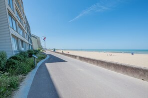 Ein gepflasterter Weg entlang eines Strandes, ein Gebäude ist links zu sehen.
