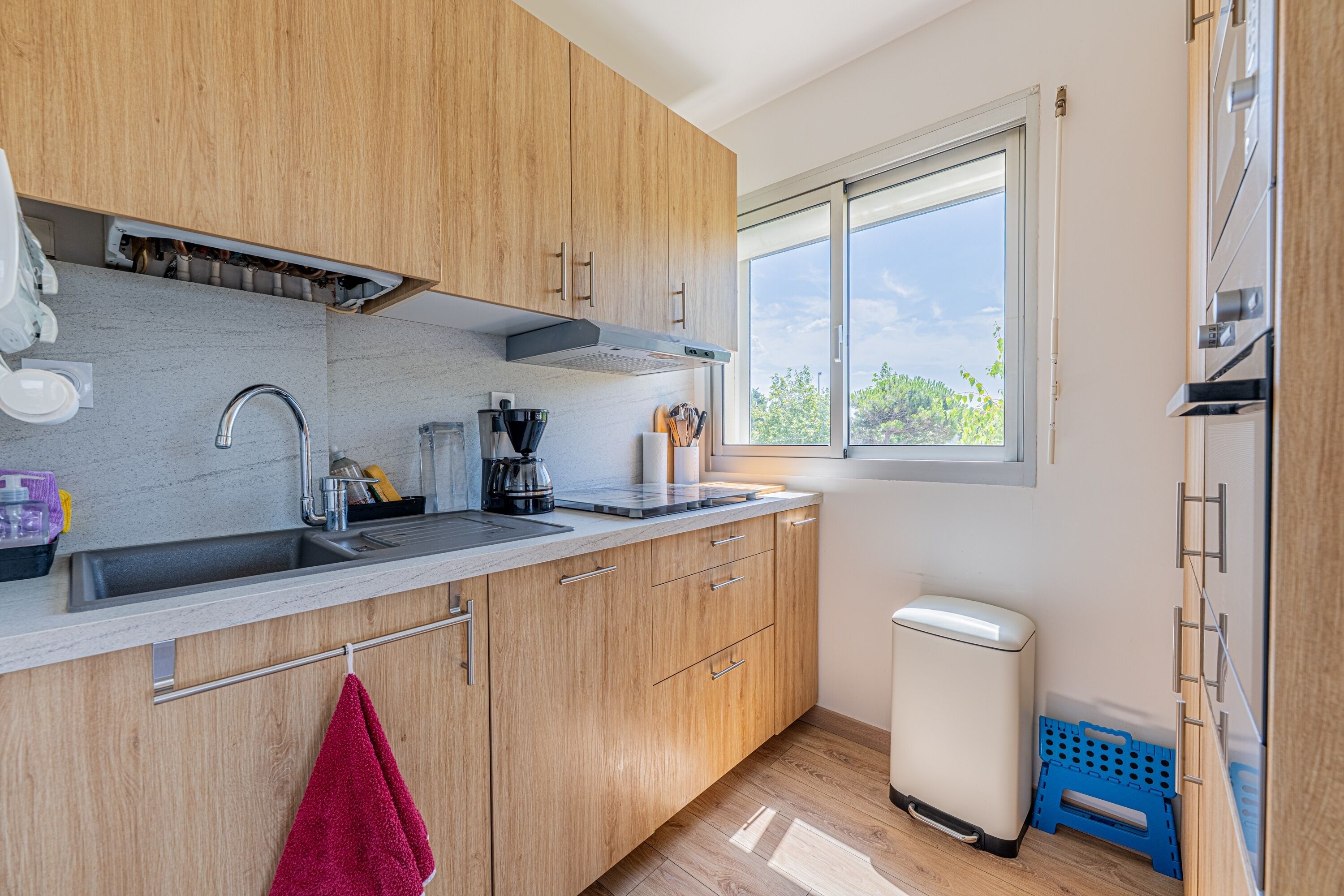 Una cocina moderna con armarios de madera, un fregadero de acero inoxidable y una ventana con vistas a la vegetación.