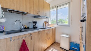 A modern kitchen with wooden cabinets, a stainless steel sink, and a window providing a view of greenery outside. - La Plage - À moins de 100 m de la plage (Courseulles-sur-Mer)