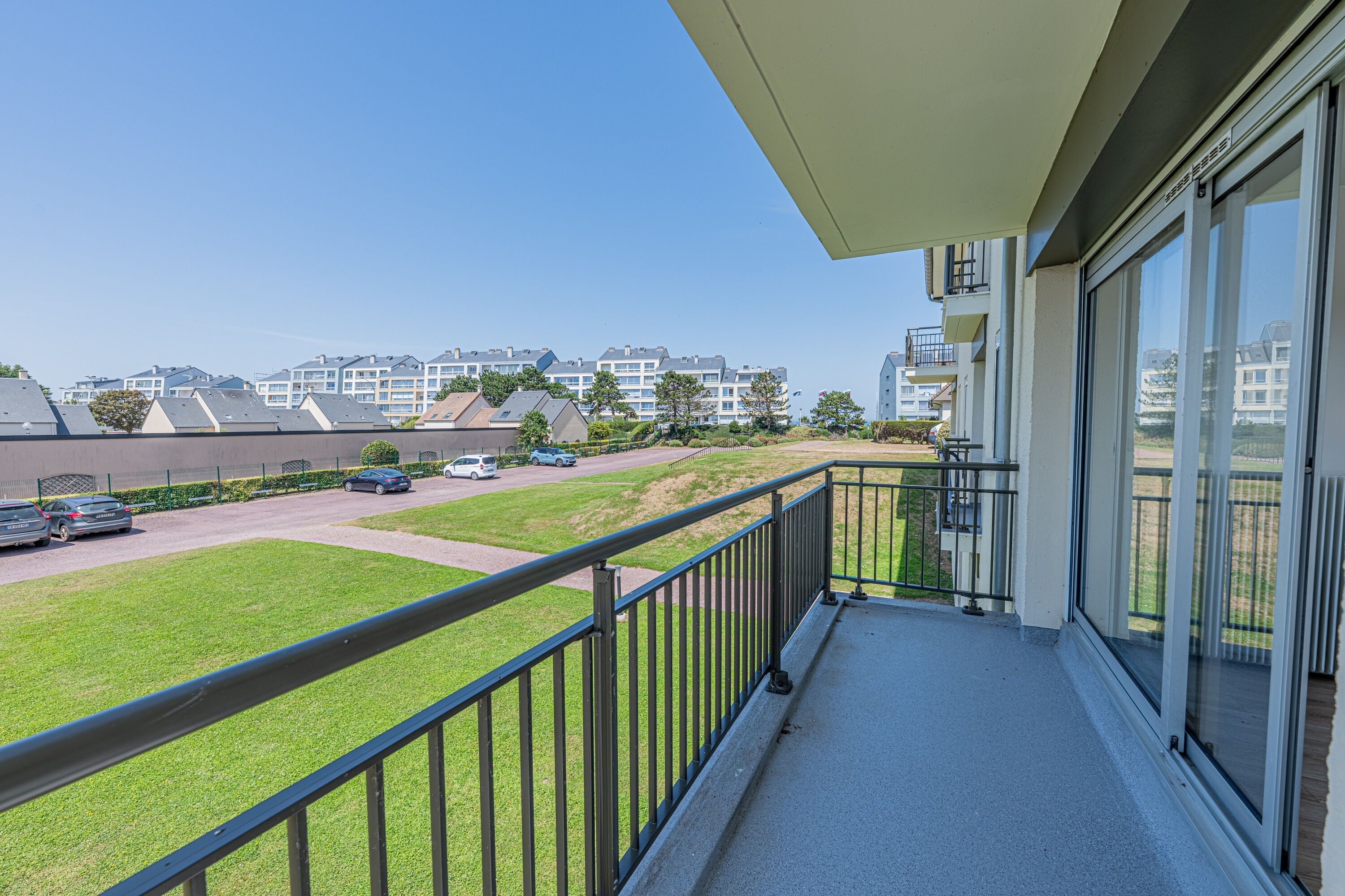 Un balcon donnant sur un parking et des immeubles d’habitation.