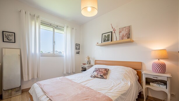 A bedroom with a bed, a bedside table, a lamp, a shelf with pictures, and a window with curtains. - La Plage - À moins de 100 m de la plage (Courseulles-sur-Mer)