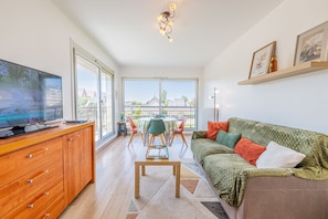 Ein modernes Wohnzimmer mit Flachbildfernseher, Holzschrank, grünem Sofa und einer Essecke mit Tisch und Stühlen.