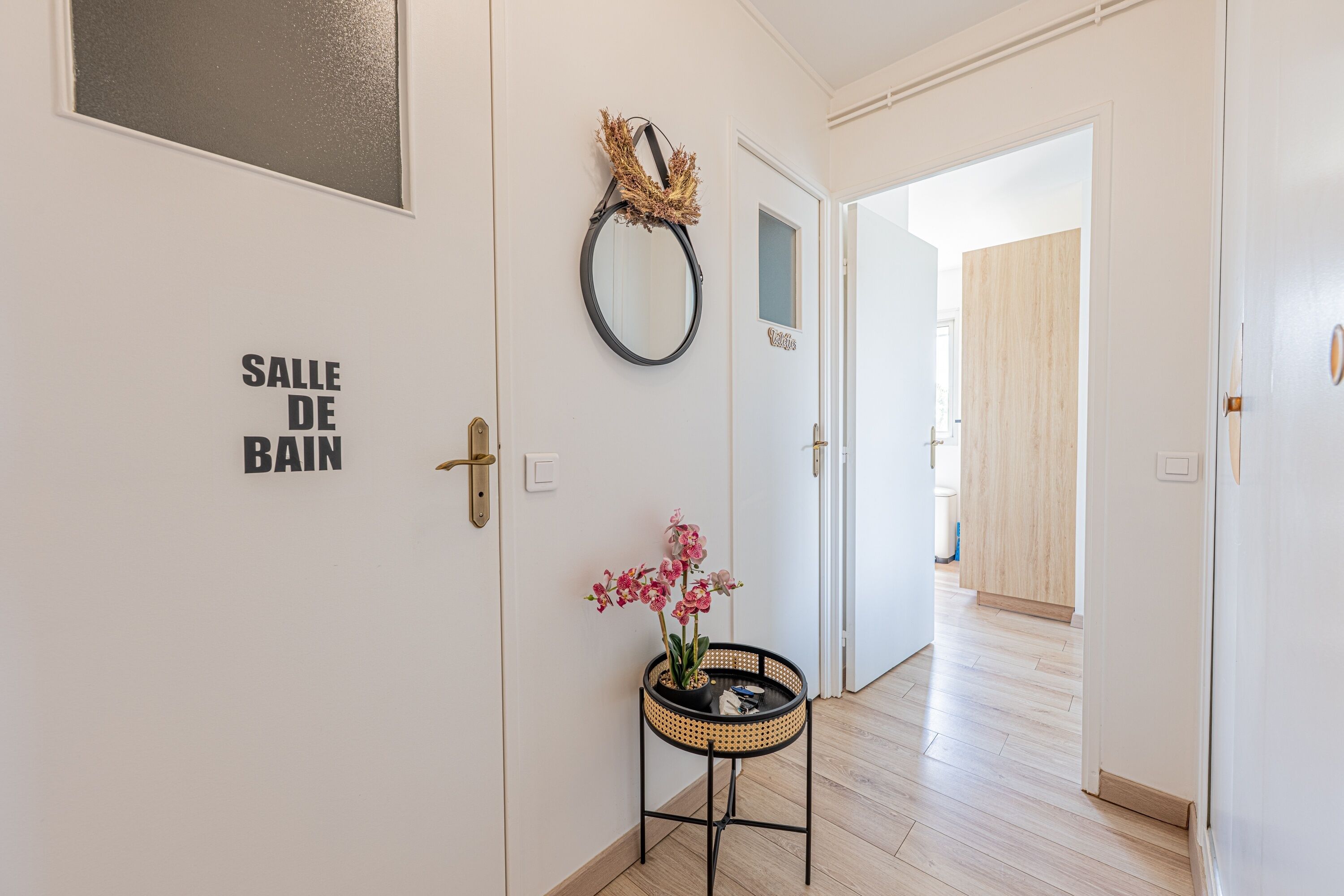 Un pasillo con una puerta que dice 'SALLE DE BAIN' y una pequeña mesa con una orquídea en maceta.