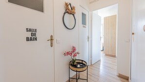 A hallway with a door labeled 'SALLE DE BAIN' and a small table with a potted orchid. - La Plage - À moins de 100 m de la plage (Courseulles-sur-Mer)