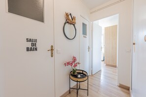 Ein Flur mit einer Tür, auf der 'SALLE DE BAIN' steht, und einem kleinen Tisch mit einer Orchidee im Topf.