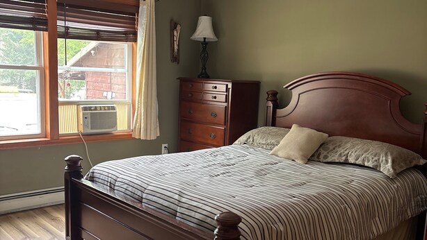 A bedroom with a wooden bed, a dresser, a lamp, and a window with blinds. - 3-bedroom campground in delightful Covington with AC comfort (Covington)