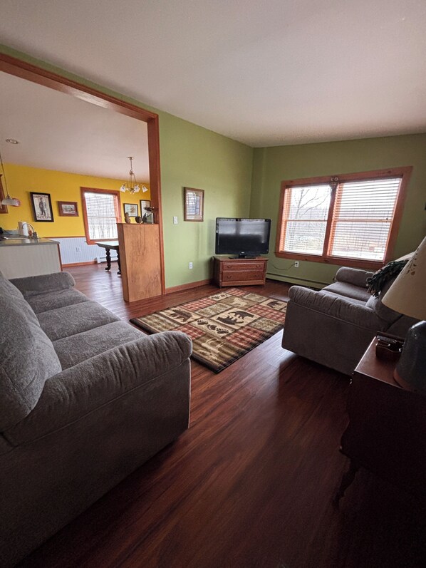 A living room with a sofa, a television, and a window with blinds.