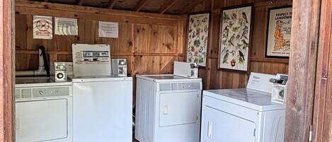 A laundry room with three white washing machines, wooden walls, and a wooden ceiling.