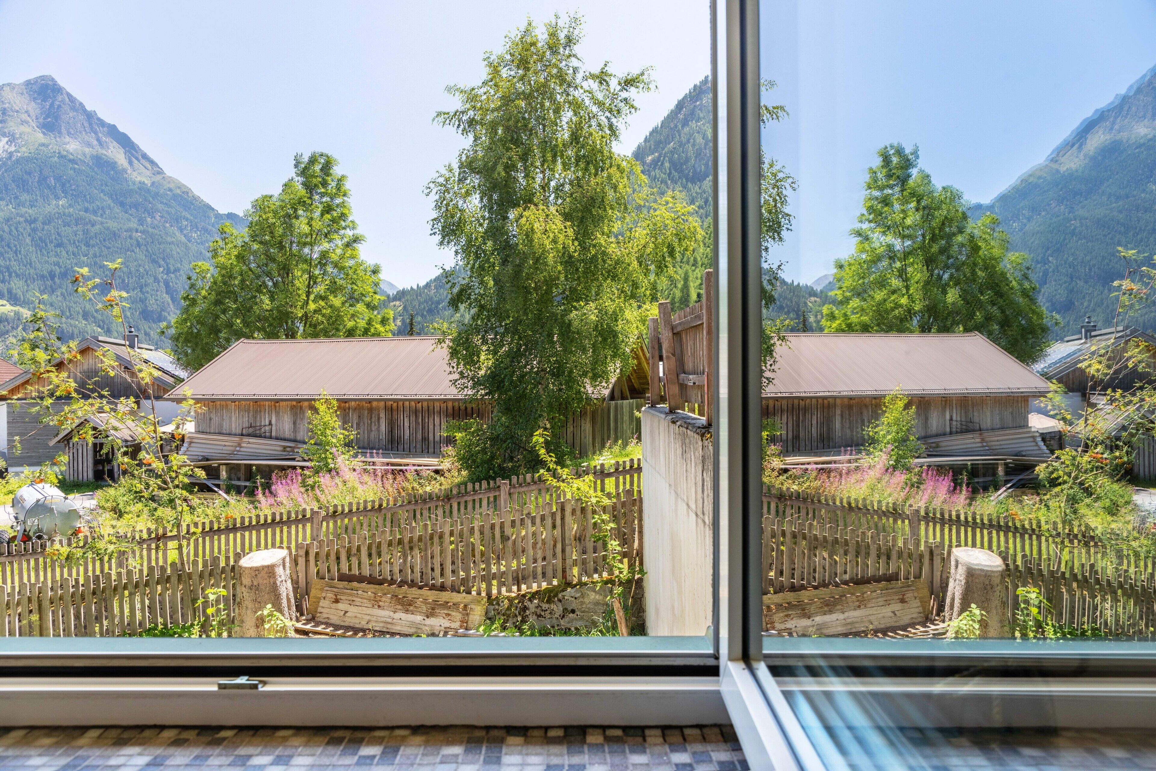 A traditional wooden building with a sloped roof, surrounded by lush greenery and mountains in the background.
