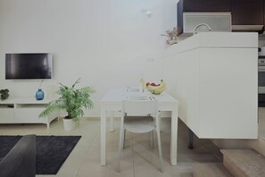 A modern kitchen with white cabinetry, a dining table with chairs, a potted plant, and a fruit bowl. - Modern Studio in a Great Location (Sliema)