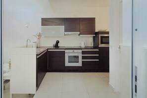 A modern kitchen with dark cabinetry, a white countertop, a built-in oven, and a microwave. - Modern Studio in a Great Location (Sliema)