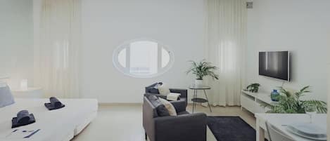 Quarto de hotel moderno com cama, sofá, mesinha, televisão e planta em vaso.