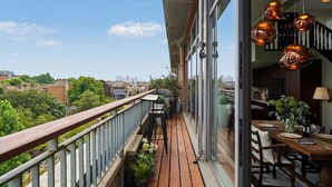 Un balcone con pavimento in legno, una zona pranzo con tavolo apparecchiato per due e vista sulla città.