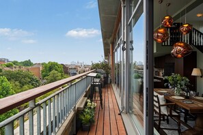 Ein Balkon mit Holzboden, einer Essecke mit Tisch für zwei Personen und Blick auf die Stadtlandschaft.