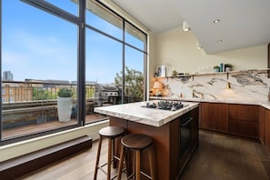 A modern kitchen with a large island, bar stools, and a view of the city. - Skyline terraces & double-height living near Borough Market (London)