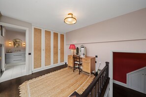 Ein Schlafzimmer mit Bett, Schreibtisch, Stuhl, Kommode, Spiegel und Deckenleuchte.