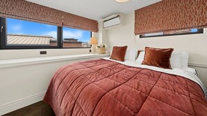 Una camera da letto con un letto grande, due finestre con tende decorate e un condizionatore d'aria, con vista sugli edifici.