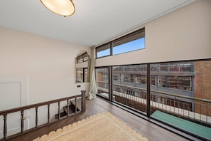 Een ruim balkon met houten reling, uitzicht op een bakstenen gebouw en een groot raam.
