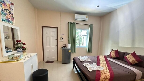 A hotel room with a bed, a desk, a mirror, a trash bin, and a window with curtains.