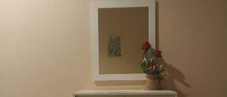 A room with a cabinet, a black ottoman, and a painting on the wall.