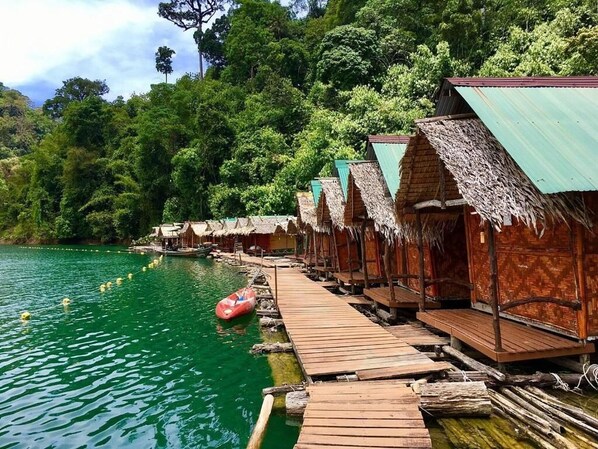 A row of thatched-roof huts with wooden walkways over water. - painting family hostel (Phanom)