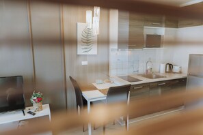 A modern kitchen with a dining area, a flat-screen TV, and a decorative plant.
