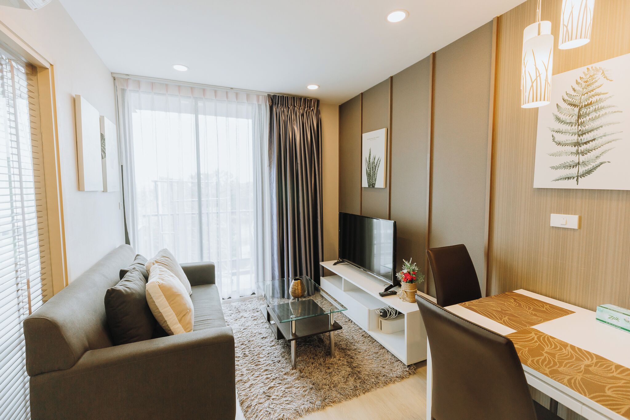 A modern living room with a sofa, a glass coffee table, a TV, and a dining area with a table and chairs.