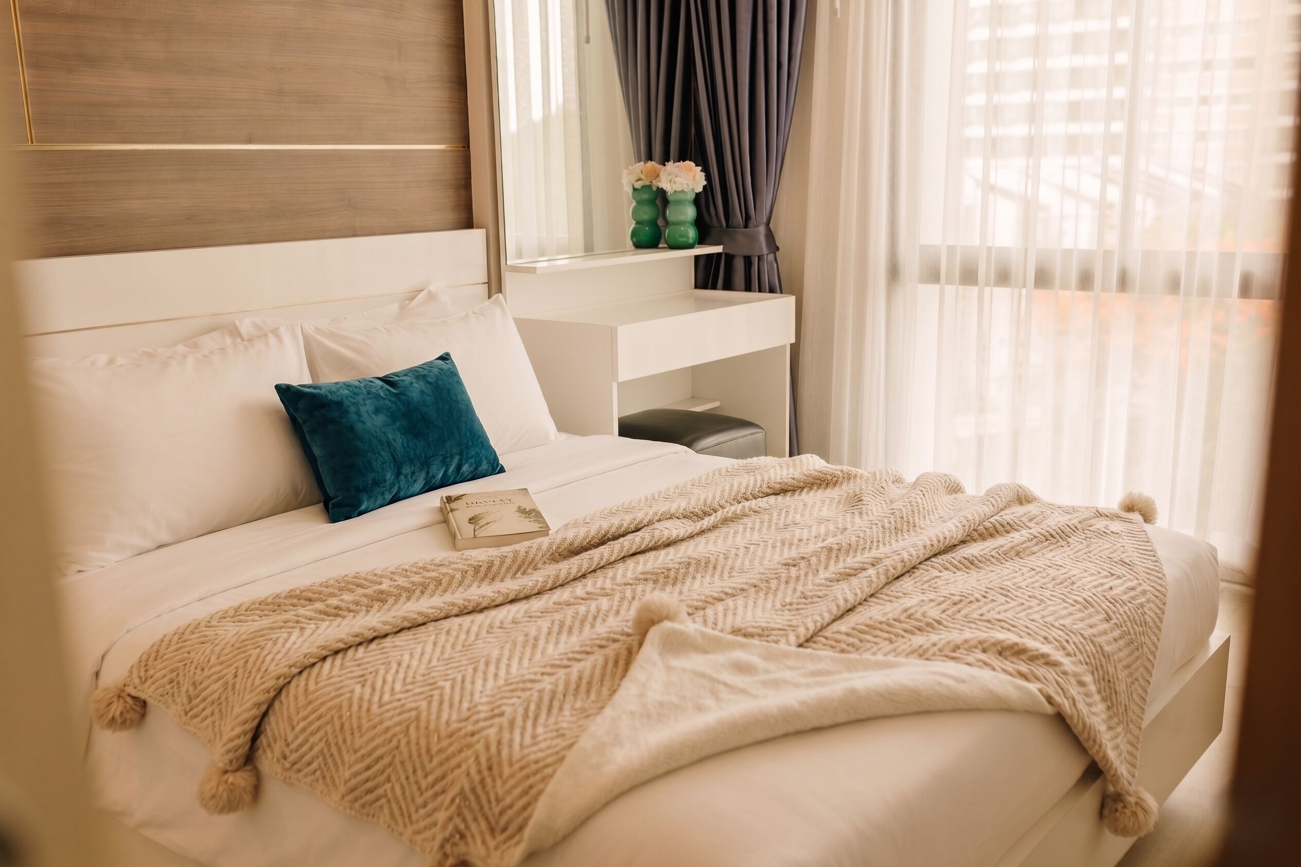 Un lit bien fait, avec une couverture beige, une tête de lit blanche et un oreiller bleu.
