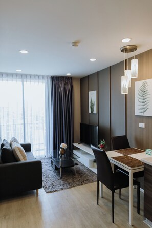 A modern living room with a sofa, dining table, and chairs, a small coffee table, and a large window with curtains.
