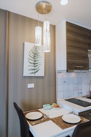 A modern kitchen with a dining area, featuring a white table, chairs, a plate of food, and a decorative fern. - 701 Cozy 1-bedroom Condo in Nimman - 4 mins walk to Maya Mall and One Nimman (Chang Wat Chiang Mai)