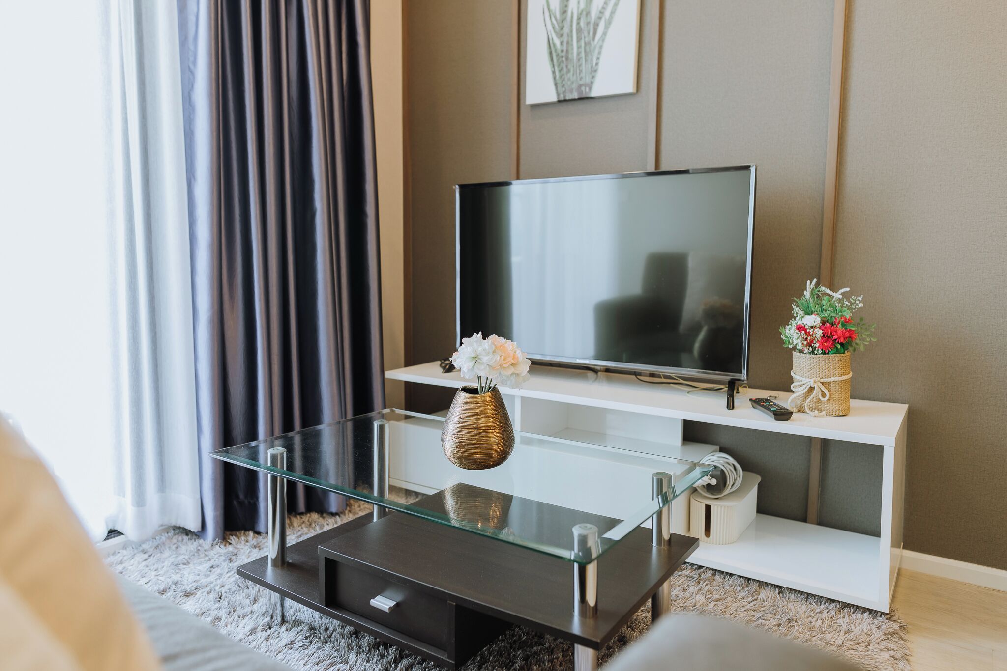 A modern living room with a flat-screen TV, glass coffee table, and decorative vases.