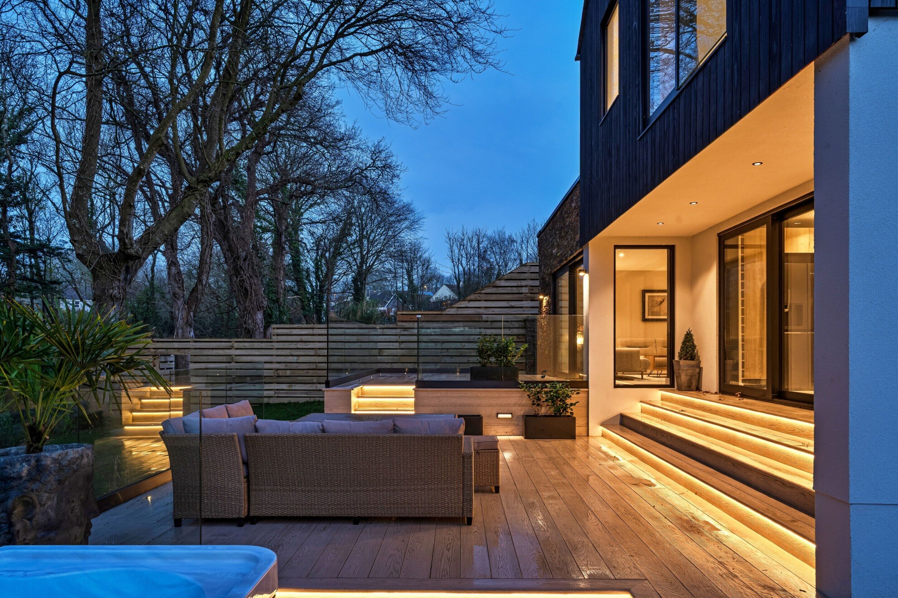 A modern outdoor living area with a wooden deck, outdoor furniture, and a staircase leading to a building.