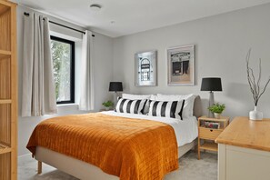 Een slaapkamer met een bed, twee nachtkastjes, een raam met gordijnen en twee aan de muur hangende foto's.