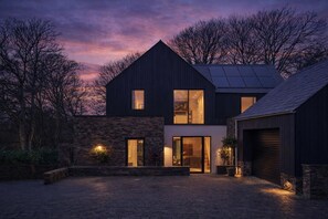 Une maison moderne à deux étages, dotée d’une façade en pierre, de grandes fenêtres et d’un garage.