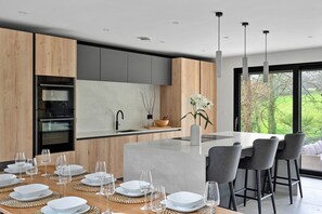 A modern kitchen with a central island, bar stools, and a dining area set for six. - Stunning Bude Retreat With Hot Tub (Bude)