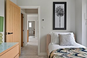 Un dormitorio con una cama, una mesita de noche, un cuadro enmarcado en la pared y una puerta que da a otra habitación.