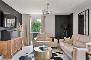 Ein modernes Wohnzimmer mit einer Sofagarnitur, einem Holzschrank, einem runden Couchtisch und einer Stehlampe.
