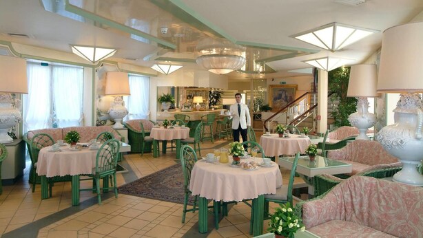 Een restaurantruimte in een hotel met meerdere tafels en stoelen, een bar en een trap.