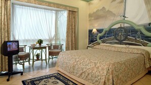 Een hotelkamer met een bed, een televisie, een klein tafeltje met stoelen en een schilderij van een roer.'