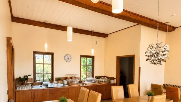 A modern kitchen with wooden cabinets, a dining area with a long table and chairs, and a cozy seating area with a sofa. - Hotel Esingerhof by Alesta (Tornesch)