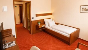 A hotel room with a bed, a desk, a chair, a nightstand, and a wall-mounted light fixture. - Hotel Esingerhof by Alesta (Tornesch)