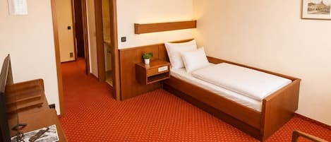 Una habitación de hotel con cama, escritorio, silla y una mesita de noche con lámpara.