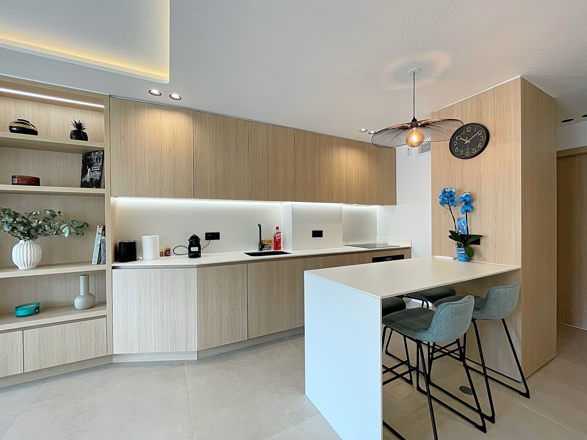 A modern kitchen with a central island, bar stools, and a clock on the wall.
