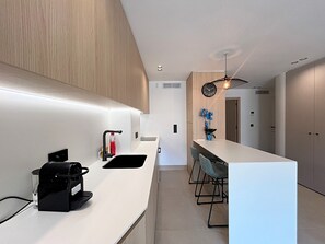 Eine moderne Küche mit weißem Arbeitsplatz, einer Kaffeemaschine und einem Spülbecken. Es gibt einen Essbereich mit Tisch und Stühlen.